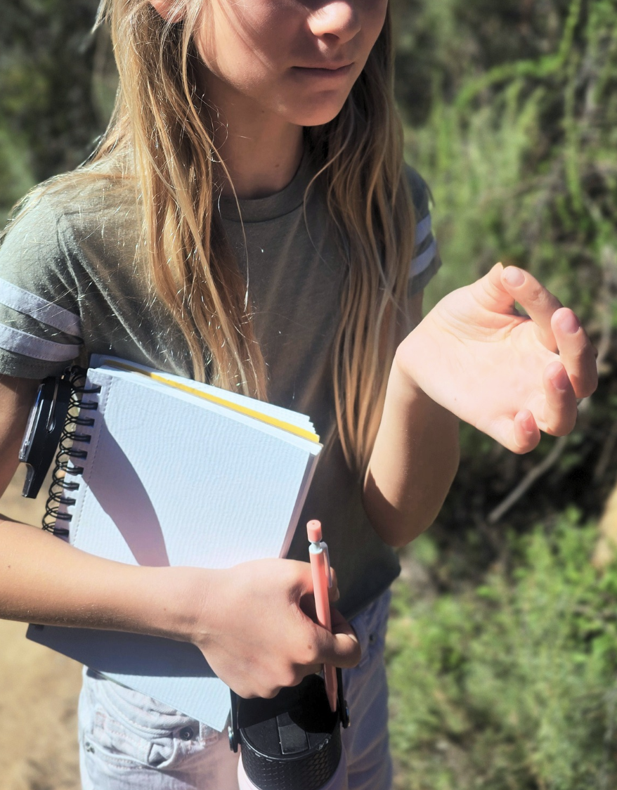 A student holding her Field Journal on a sunlit trail.